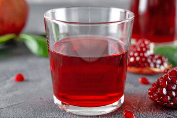 A glass of pomegranate juice with fresh pomegranate fruits on a gray concrete background. Vitamins and minerals. Healthy drink concept. Copy space.