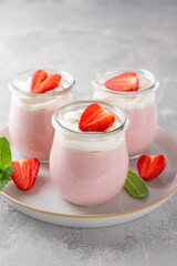 Strawberry mousse in a glass jar on a gray concrete background with whipped cream, fresh berries and mint leaves. Delicious summer dessert.