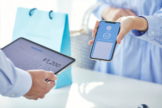 スマートフォンを持ちキャッシュレス決済をする女性の手元と店員の手