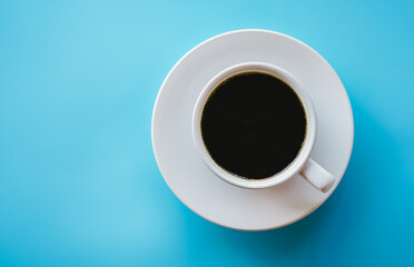 Top view of hot coffee in white coffee cup on blue background with copy space