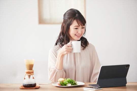 コーヒーを飲みながらタブレット端末を見る女性