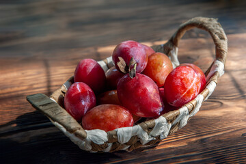 wicker basket filled with red plums on a rustic table. photographed in natural light in real life