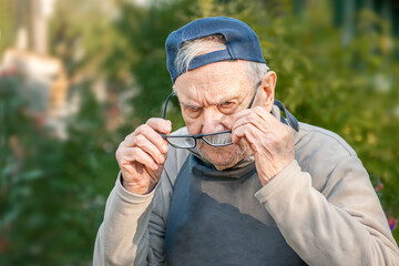 an 88-year-old man in a baseball cap puts on glasses. Portrait of an old farmer with glasses in the garden