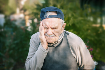 Portrait of an 88-year-old man with a headache or toothache. farmer is working in the garden. copy...