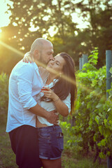 Portrait of a Smiling  happy Couple Kissing    in a Vineyard toasting wine. Beautiful  brunette woman and bearded muscular man spending time together during grape harvest.