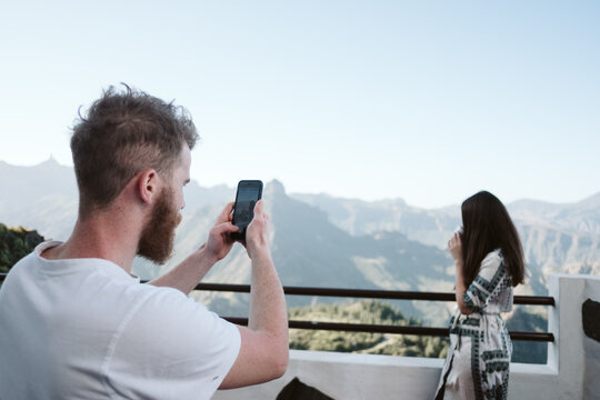 Man taking mobile photos of his girlfriend in a mountainous landscape