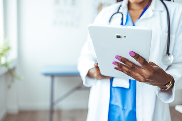 Close up of woman doctor hands using digital tablet at clinic. Closeup of female doctor in labcoat and stethoscope holding digital tablet, reading patient report. 