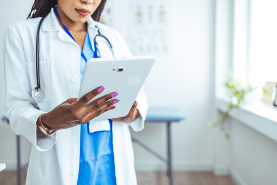 Shot of a young doctor using her digital tablet at work. Young female clinician in whitecoat and eyeglasses using touchpad while communicating with patients online. Doctor using digital tablet - Powered by Adobe