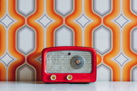 Red vintage radio on table against wall with white and orange geometric shapes