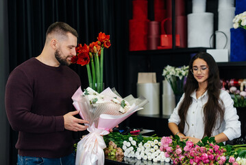 A young bearded man buys a beautiful bouquet of flowers for a girl's holiday in a cozy flower shop. Floristry and bouquet making in a flower shop. Small business.