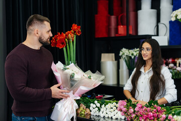 A young bearded man buys a beautiful bouquet of flowers for a girl's holiday in a cozy flower shop. Floristry and bouquet making in a flower shop. Small business.