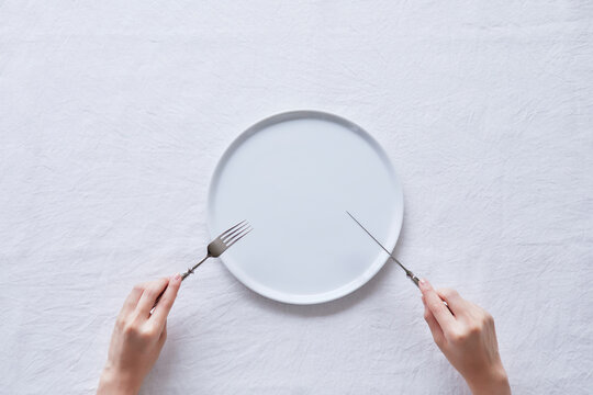 白い皿とナイフとフォークを持つ女性の手