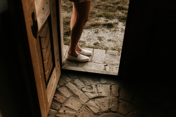 A woman is standing outside the threshold of a door. Rustic vintage stone brick pavement inside and...