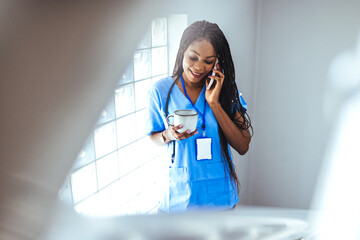 Female doctor drinking coffee on hospital background. Portrait of smiling nurse drinking coffee. Carrying coffee, a female nurse in the clinic open as she have break. - obrazy, fototapety, plakaty