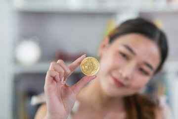 Asian woman girl smiling holding gold bitcoin crypto currency blockchain on wood table desk in...