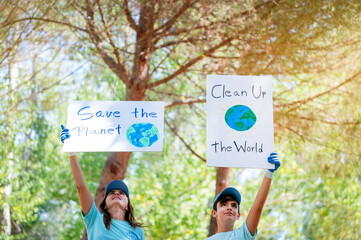 Woman and child volunteers picking up litter and holding a Clean Up the World and save the planet sign in a park
