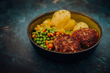 Meatballs of minced pork on mixed vegetables of carrots and peas with potatoes in a bowl and with a dark background