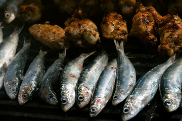 Top view of sardines and chicken cooking on the grill