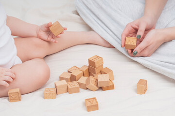 Mom and child are learning the English alphabet, close-up. The child plays with wooden cubes, with English letters. The concept of early development, preschool education at home. Educational games