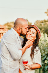 Portrait of a Smiling  happy Couple Kissing    in a Vineyard toasting wine. Beautiful  brunette woman and bearded muscular man spending time together during grape harvest.