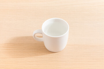 Cup of water isolated on wood background. Drinking water. White mug. Beverage. Wooden surface. Simplicity. Minimalist object.
