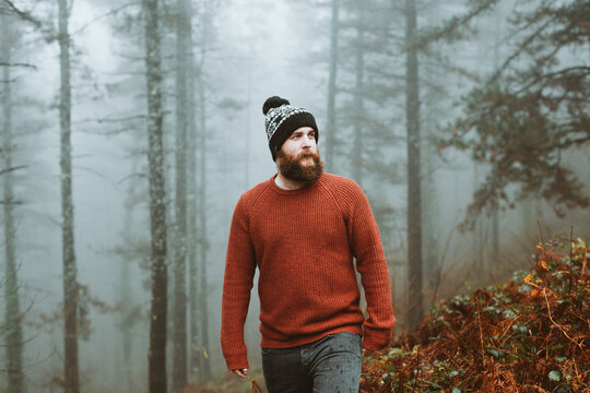 Bearded guy in sweater and hat near fir trees