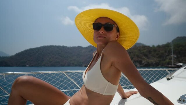 Beautiful woman wearing straw hat and white bikini on a yacht enjoys the journey. High quality 4k footage