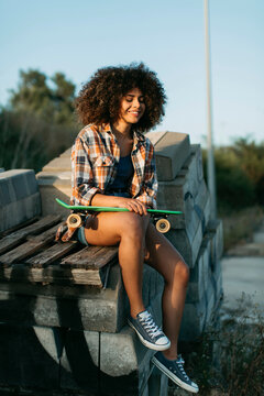 African American woman with penny board sitting on stones on the street