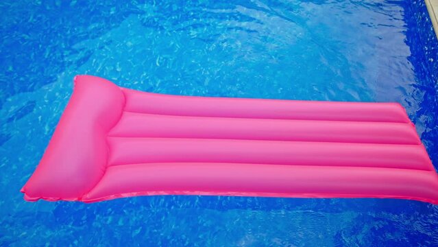 Pink swimming mattress moving by the pink surface of water. Inflatable mattress in the swimming pool. Top view.