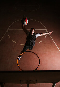 Strong determined man playing basketball on court at night