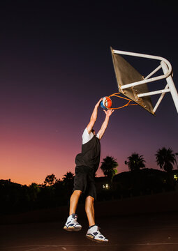 Strong determined man playing basketball on court at night