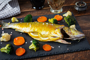 Baked sea bass fish with vegetables and greens on stone plate