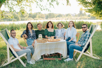 Group of friends are relaxing together outdoor. Young cheerful people looking at the camera.
