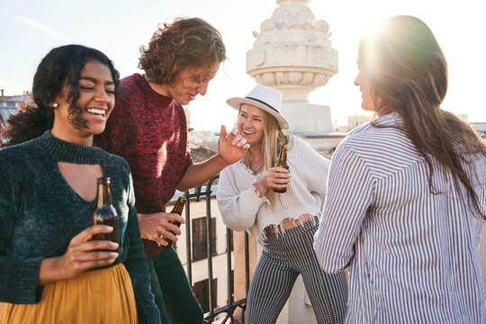 Joyful diverse friends with beer dancing on rooftop