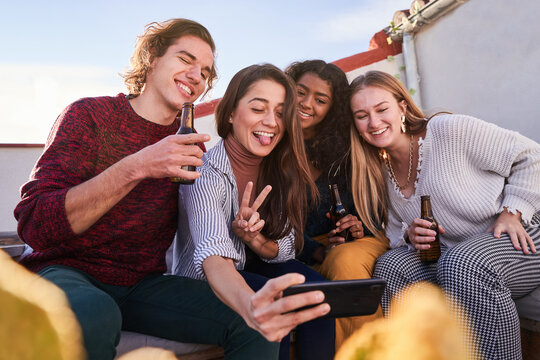 Joyful diverse friends taking selfie during party on terrace