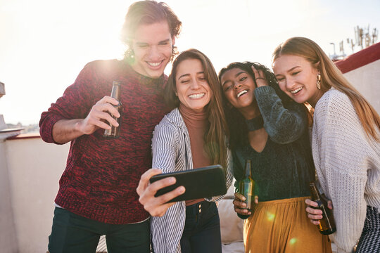 Joyful diverse friends taking selfie during party on terrace