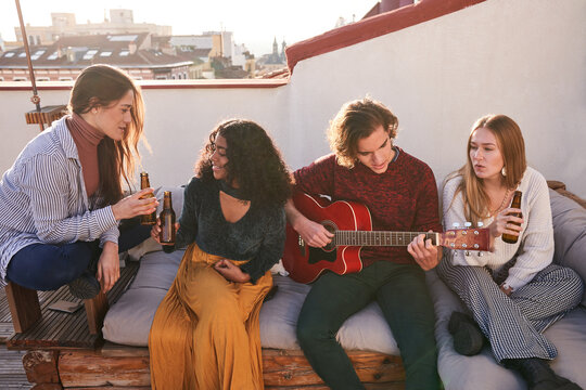 Cheerful diverse friends gathering on terrace and playing guitar - Powered by Adobe