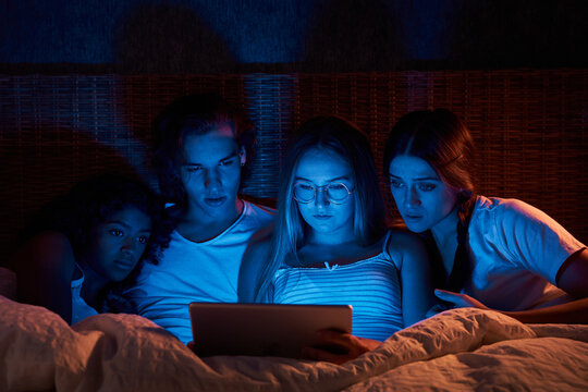Scared flatmates watching horrors in dark bedroom