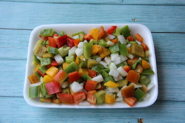 Mixed colored peppers, chopped in a styrofoam tray, practicality in the kitchen on wooden table, top view. Space for text. (Capsicum annuum).