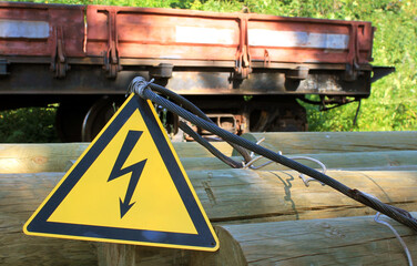 Caution electricity sign on wooden bars against the background of a railway cargo platform, High voltage icon, danger symbol, Attention, electricity danger symbol, electricity warning triangular symbo