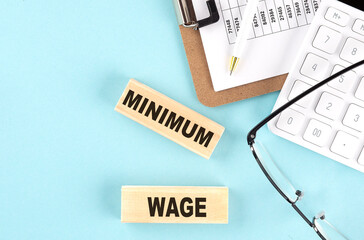 MINIMUM WAGE text written on wooden block with clipboard,eye glasses and calculator Business...