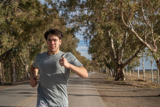 young man running in the street with trees