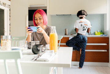 Cheerful young woman using smartphone near cooking black friend