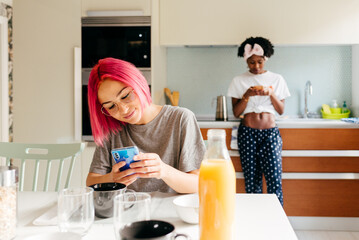 Cheerful young woman using smartphone near cooking black friend