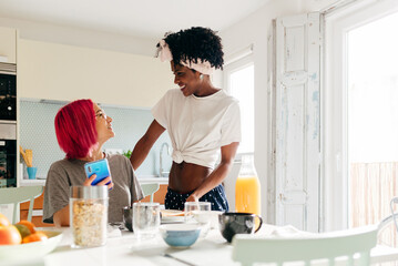Cheerful young woman using smartphone near cooking black friend