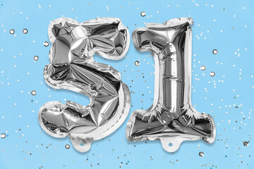 Silver foil balloon number, digit fifty one on a blue background with sequins. Birthday greeting...
