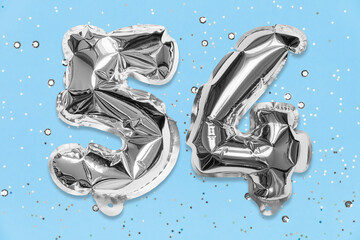 Silver foil balloon number, digit fifty four on a blue background with sequins. Birthday greeting...