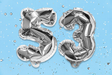 Silver foil balloon number, digit fifty three on a blue background with sequins. Birthday greeting...