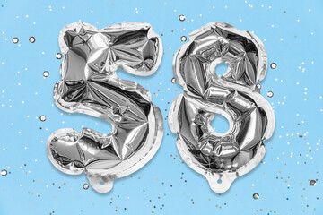 Silver foil balloon number, digit fifty eight on a blue background with sequins. Birthday greeting card with inscription 58. Top view. Numerical digit. Celebration event, template.