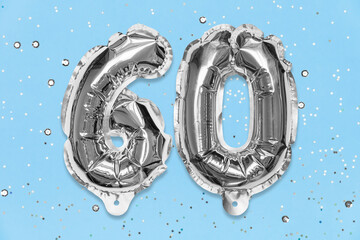 Silver foil balloon number, digit sixty on a blue background with sequins. Birthday greeting card with inscription 60. Anniversary concept. Top view. Numerical digit. Celebration event, template.